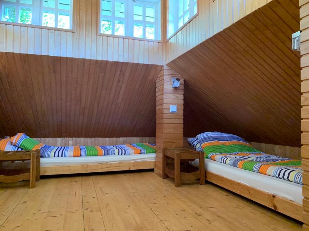 two beds in a room with wooden walls and windows at Alėjos Namelis in Palanga