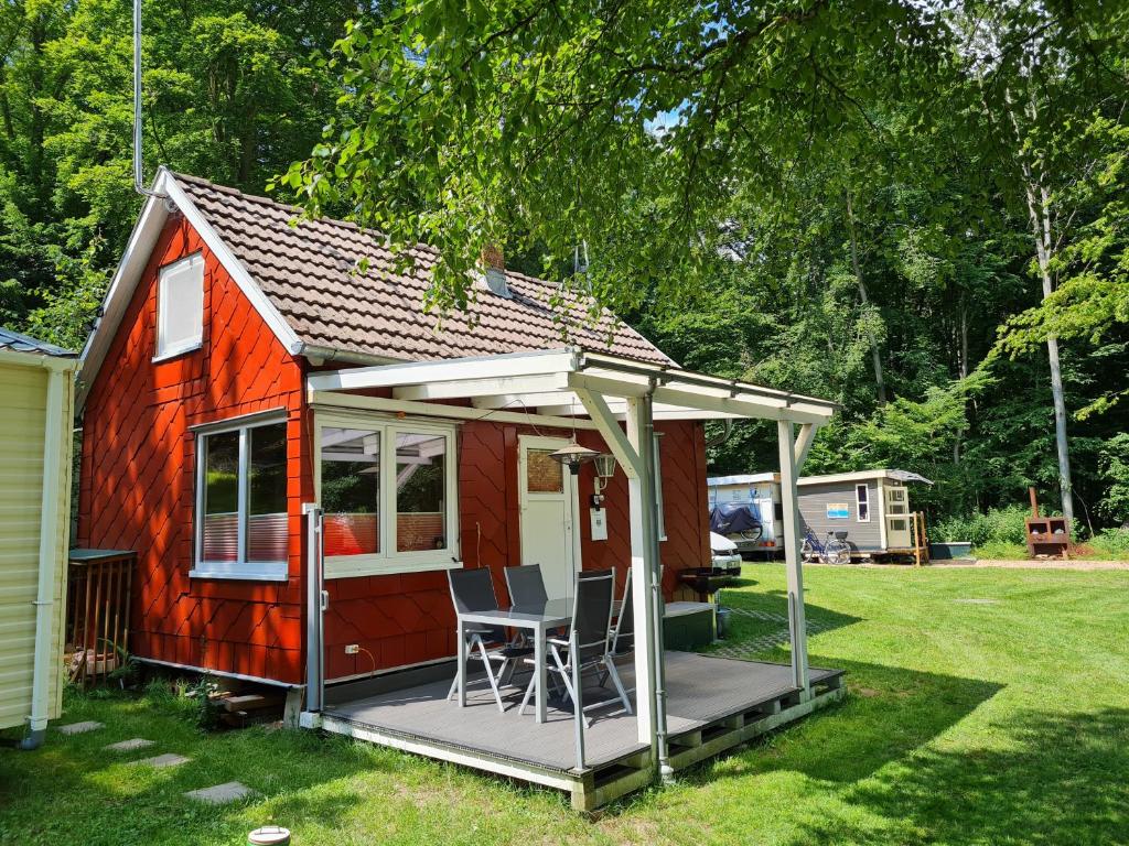 Una pequeña casa roja con porche y sillas. en Ferienhaus direkt am Badesee Bungalow 11 Schönsee, en Urnshausen