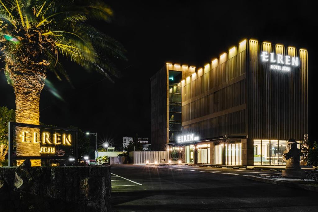 a building with a palm tree in front of it at night at Elren Hotel Jeju in Seogwipo