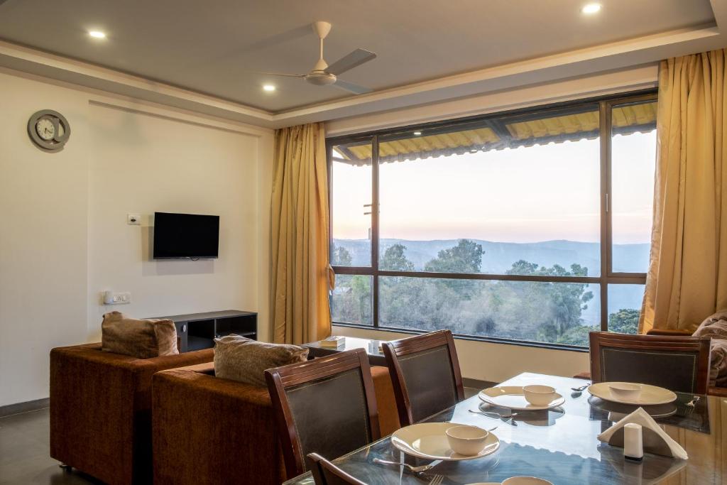 a living room with a table and a large window at West Valley 3BHK Mahabaleshwar in Mahabaleshwar