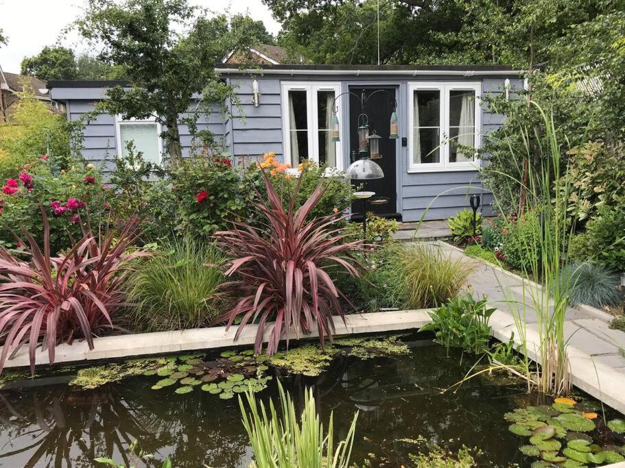 a tiny house with a pond in front of it at Lovely detached garden chalet in Broadstone
