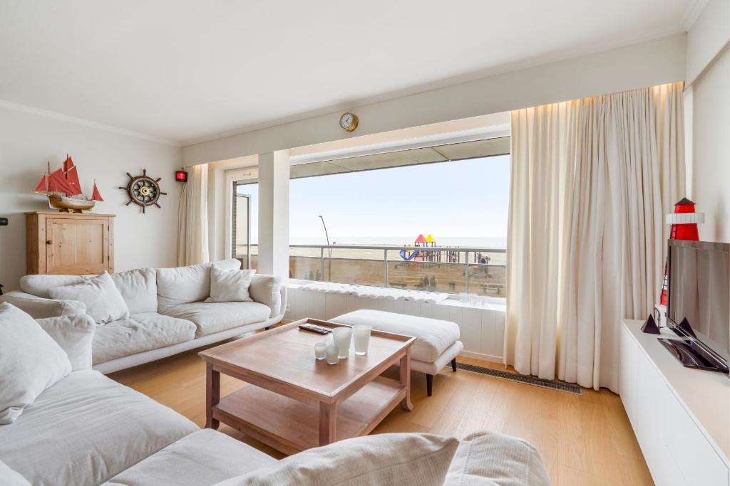 ein Wohnzimmer mit weißen Möbeln und einem großen Fenster in der Unterkunft Kindvriendelijk app met frontaal zeezicht &garage in Koksijde