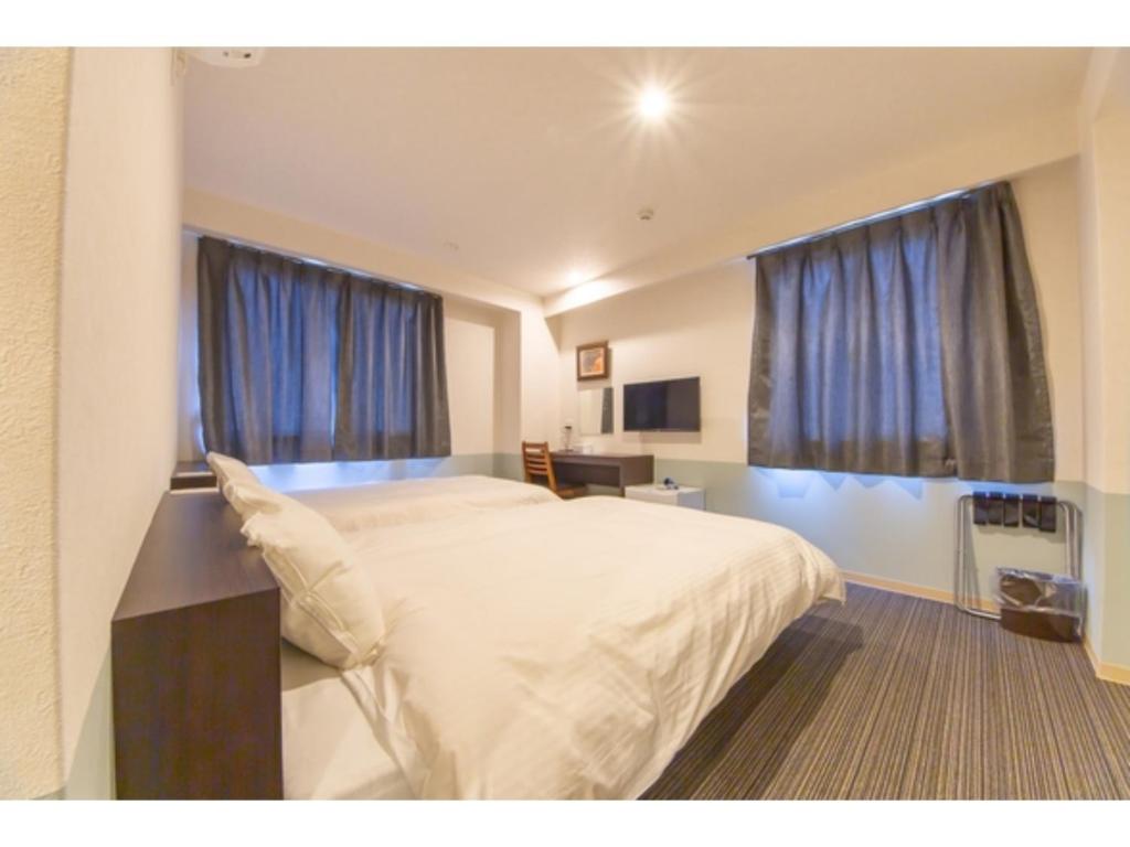 1 dormitorio con 1 cama blanca grande y cortinas azules en Hotel Taiyonoen Tokushima Kenchomae - Vacation STAY 26351v, en Tokushima