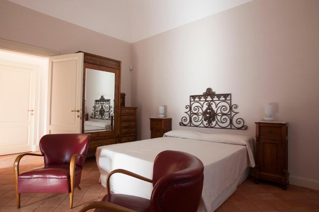 a bedroom with a bed with two chairs and a mirror at Il Melograno in San Leonardello
