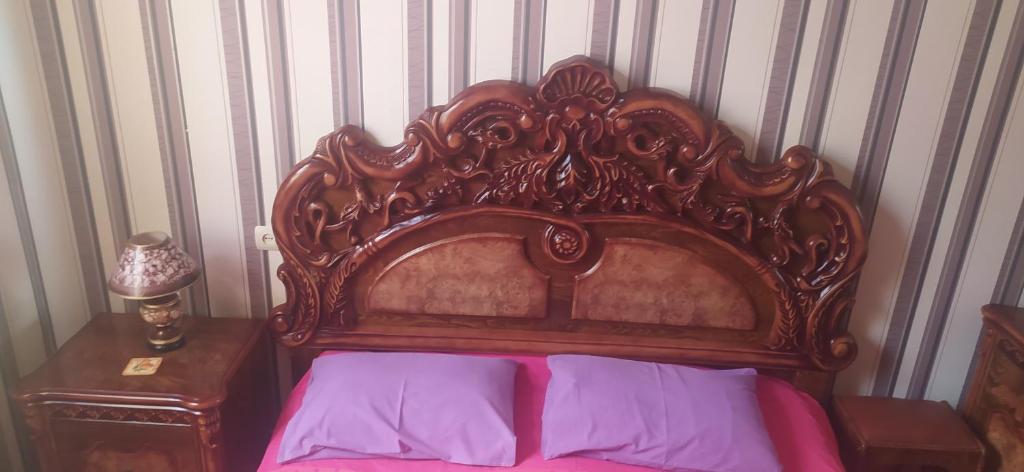 uma cama com uma cabeceira de cama de madeira ornamentada com lençóis roxos em GEO Vake Guest House em Tbilisi