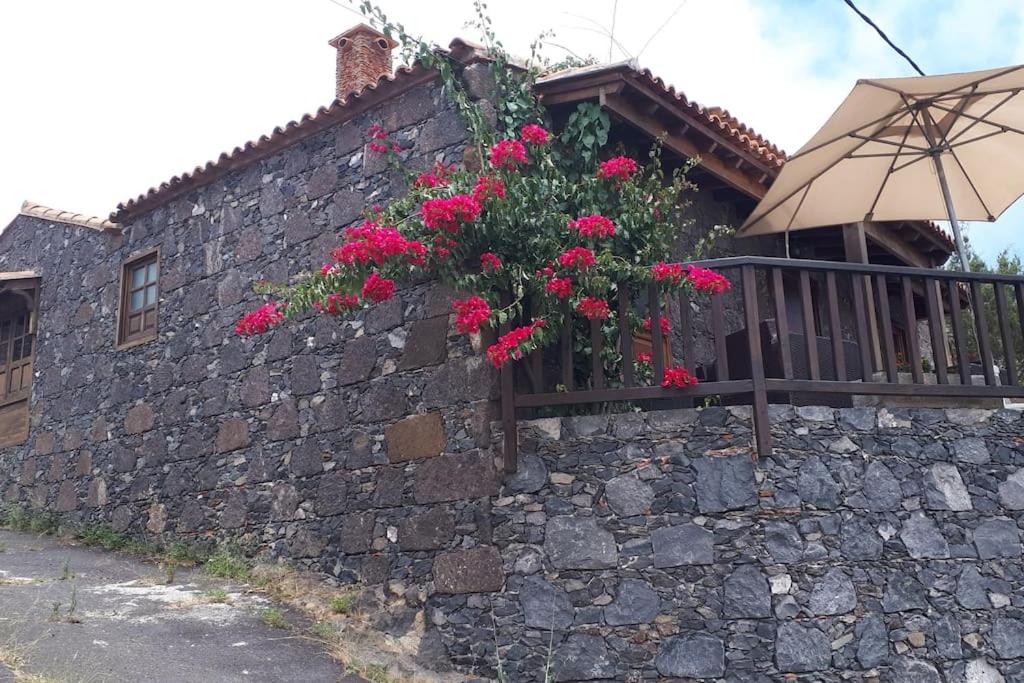 a stone wall with flowers on a balcony with an umbrella at Casa Tía Rosa. in Adeje