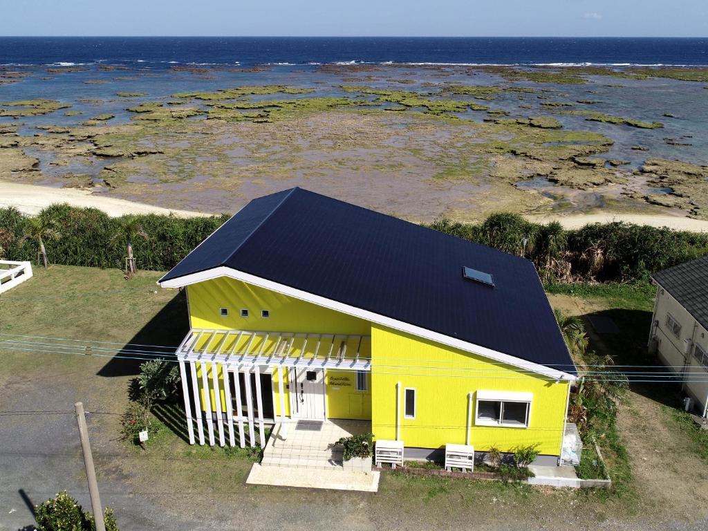 ein gelbes Haus mit schwarzem Dach und Meer in der Unterkunft オーシャンヴィラ徳之島-Ocean Villa Tokunoshima- in Tokunoshima