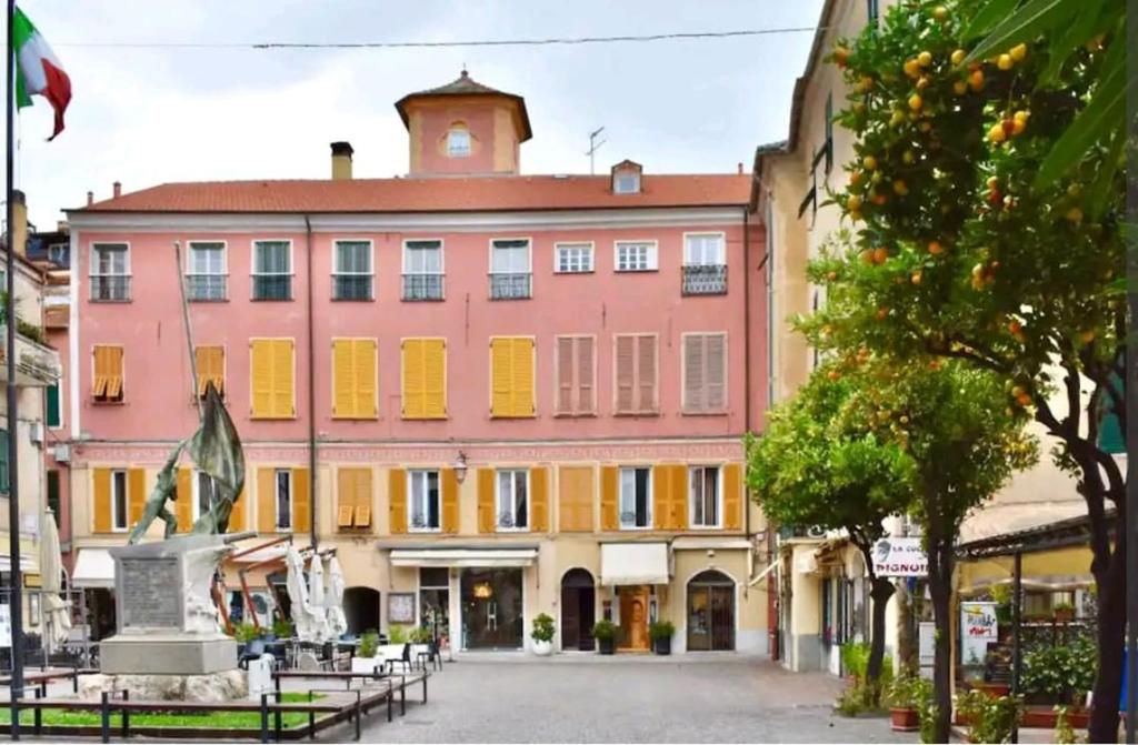 un gran edificio rosa con persianas amarillas en una calle en Appartamento magico nel centro del borgo L'ancora., en Laigueglia