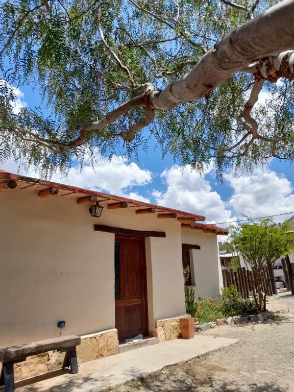 una pequeña casa blanca con una puerta de madera bajo un árbol en Cactus y Almacen - Purmamarca en Purmamarca