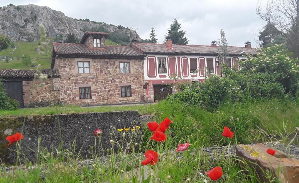 una casa de piedra con flores rojas delante de ella en Casa Entrenidos en Mudá