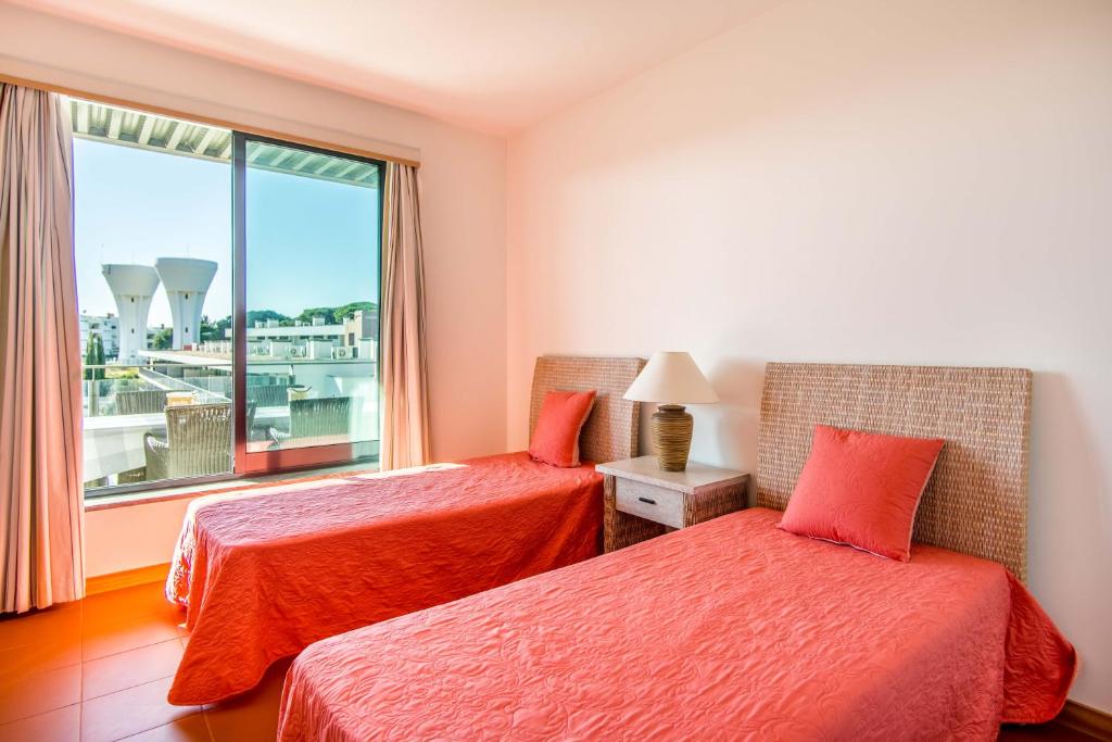 two beds in a room with a window at Superbe appartement spacieux avec terrasse vue piscine in Vilamoura