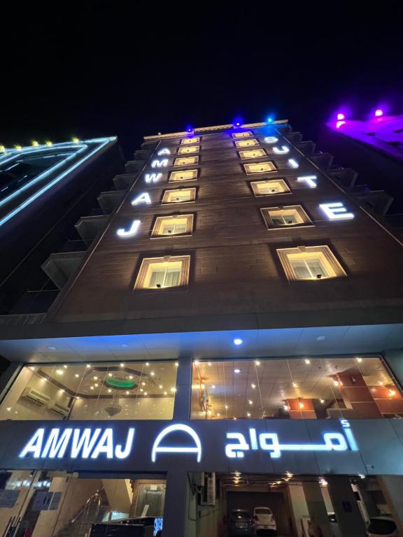 a tall building with an amazon ale sign at night at أمواج للشقق المخدومة - FoR SERVICED APARTMENTS in Al Jubail