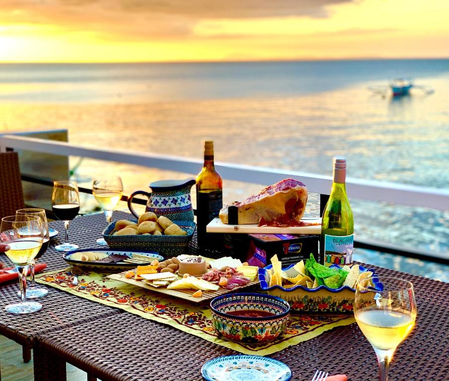 PamAnilao and Padoy's Dive Camp في باتانجاس سيتي: طاولة مع الطعام والنبيذ على شرفة مع المحيط