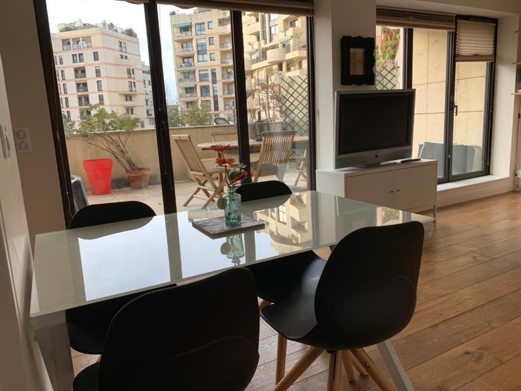 einen Glastisch und Stühle in einem Wohnzimmer mit einem TV in der Unterkunft Superbe appartement 3 pièces 57 m2 avec Terrasse 33m2 in Levallois-Perret