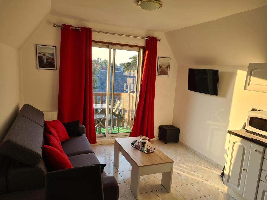 sala de estar con sofá y ventana con cortinas rojas en Charmant studio proche de la mer, en Tourgéville