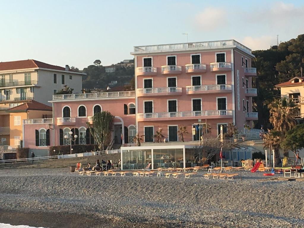 een roze gebouw met tafels en stoelen ervoor bij Hotel Piccolo Lido in Bordighera