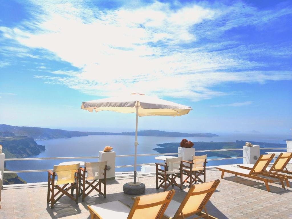 einer Gruppe von Stühlen und einem Regenschirm auf einer Terrasse in der Unterkunft Artemisia Apartment Caldera in Imerovigli