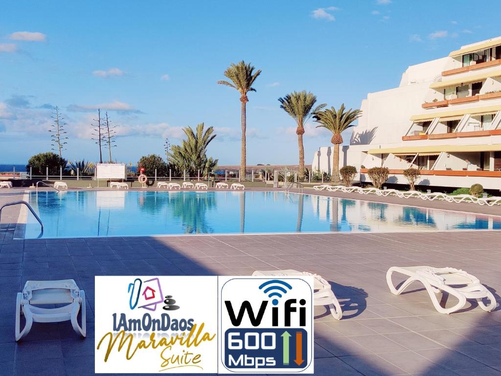 une piscine avec des chaises et un panneau en face d'un bâtiment dans l'établissement MARAVILLA Suite 140 m2 - 3 Bedrooms, Heated Pool, à Costa del Silencio