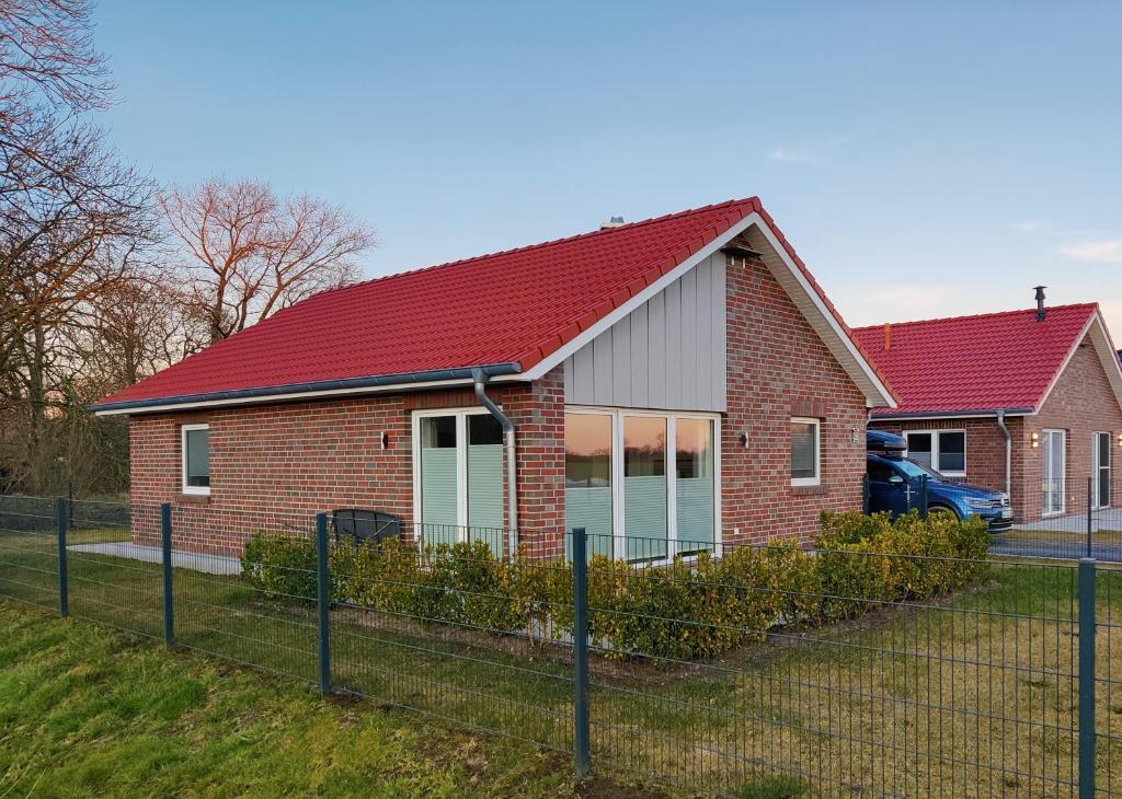 una casa di mattoni con un tetto rosso e una recinzione di Haus MeerErleben - Urlaub mit Hund an der Nordsee a Schweiburg