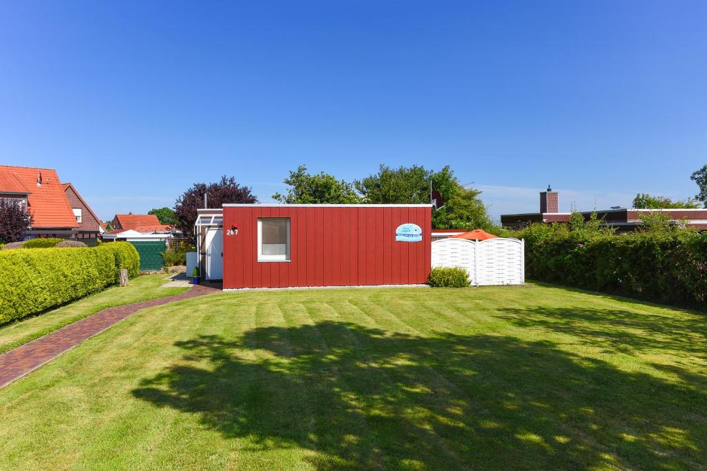 ein roter Schuppen in einem Hof mit einem Grasfeld in der Unterkunft Ferienhaus Ingrid in Bensersiel