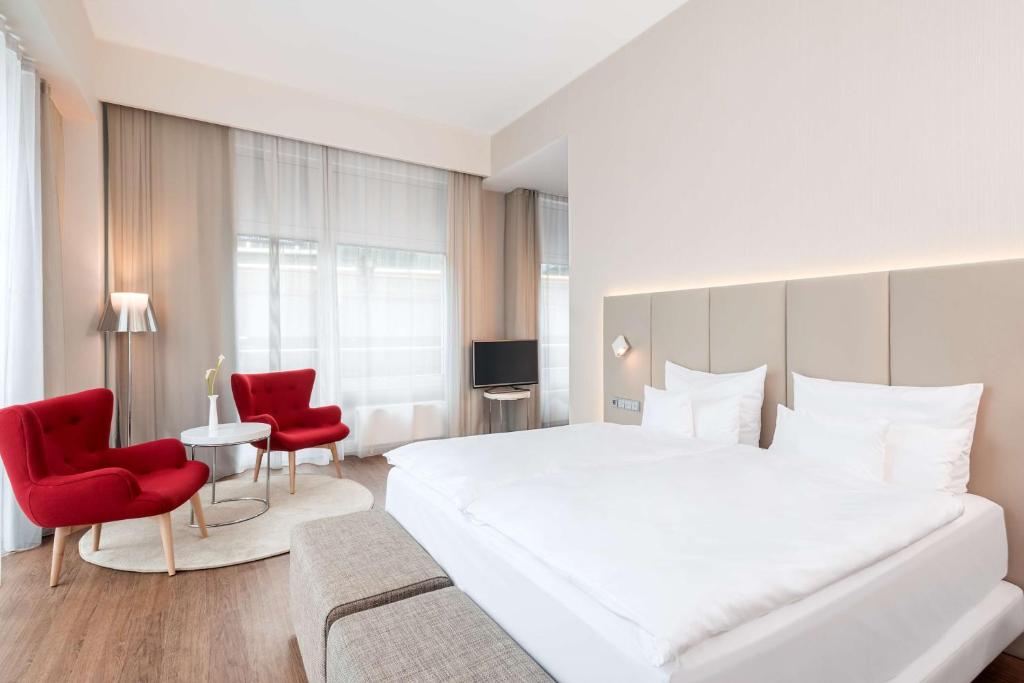 a bedroom with a large white bed and red chairs at NH Collection Berlin Mitte Friedrichstrasse in Berlin