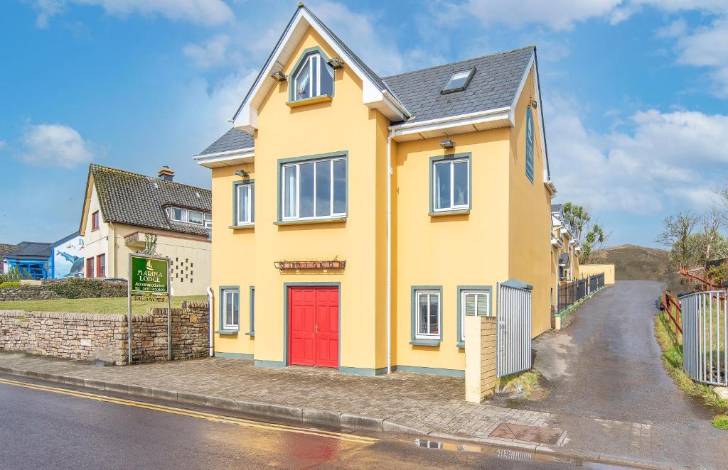 a yellow house with a red door on a street at Dingle Marina Lodge in Dingle