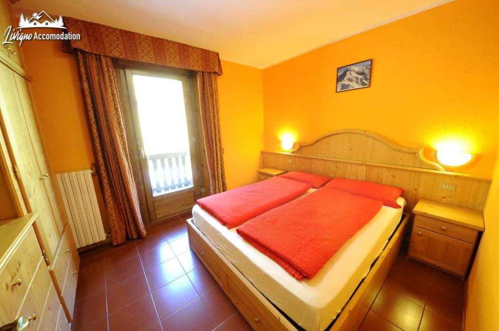 ein Schlafzimmer mit einem Bett mit orangefarbener Bettwäsche und einem Fenster in der Unterkunft Casa Florin Giumel con vista sulle piste da sci in Livigno