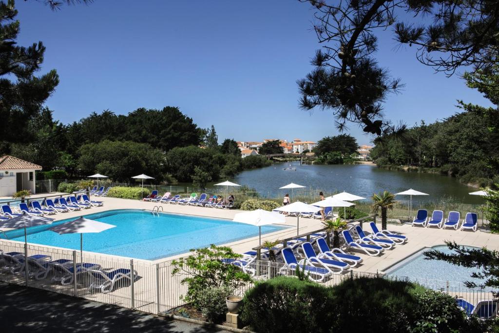 une piscine avec des chaises et des parasols et un lac dans l'établissement Belambra Clubs Saint-Jean-de-Monts - Les Grands Espaces, à Saint-Jean-de-Monts