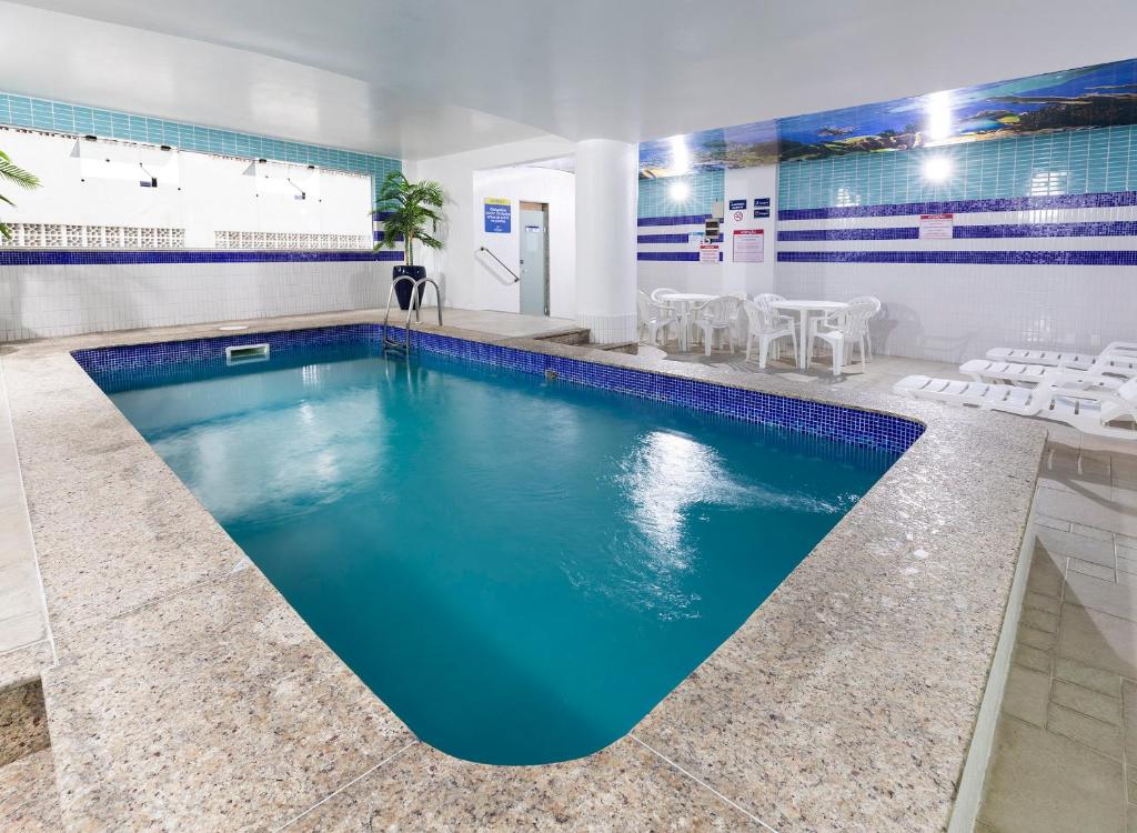 a pool with blue water in a room with white chairs at Centromar Hotel in Balneário Camboriú