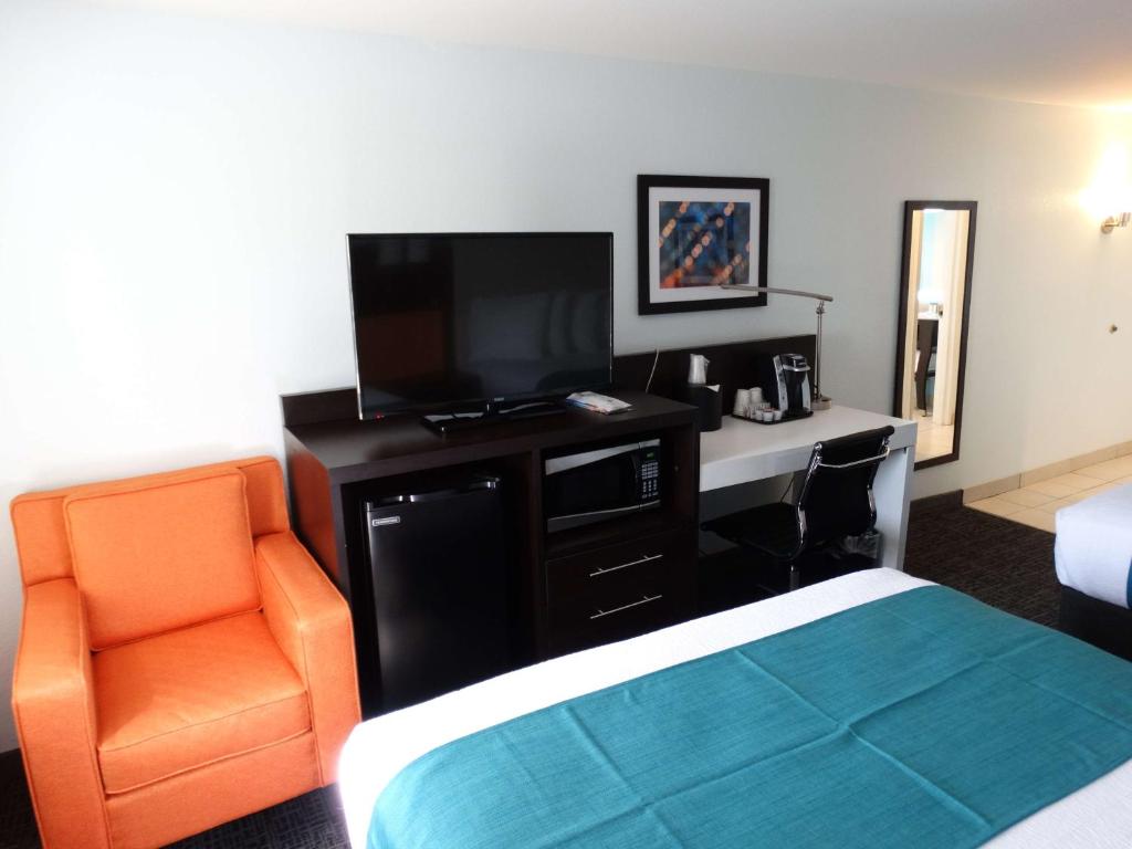 a hotel room with a bed and a television and a chair at Best Western Plus Orlando Lake Buena Vista South Inn & Suites in Kissimmee