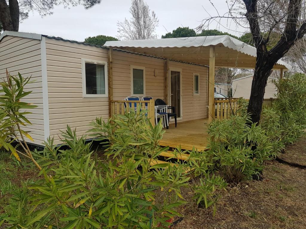 une petite maison avec une terrasse couverte et une terrasse dans l'établissement Mobil Home 6 à 8 personnes Camping Vagues Océanes L'Elysée, au Grau-du-Roi