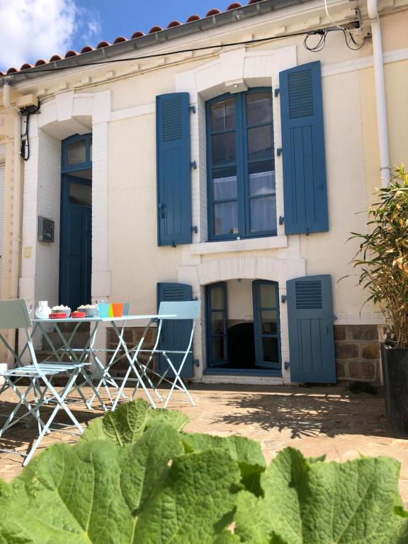 ein Haus mit blauen Fensterläden sowie einem Tisch und Stühlen in der Unterkunft Maison de pêcheur située dans une impasse privée à 300 m de la mer in Les Sables-dʼOlonne