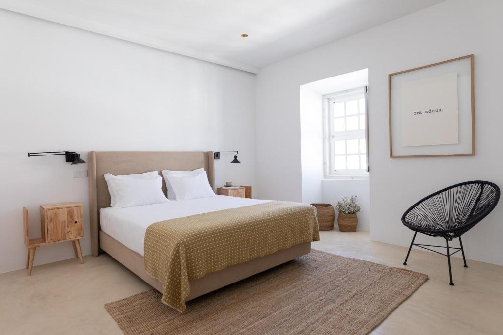 a white bedroom with a bed and a chair at Casa do Gadanha in Estremoz