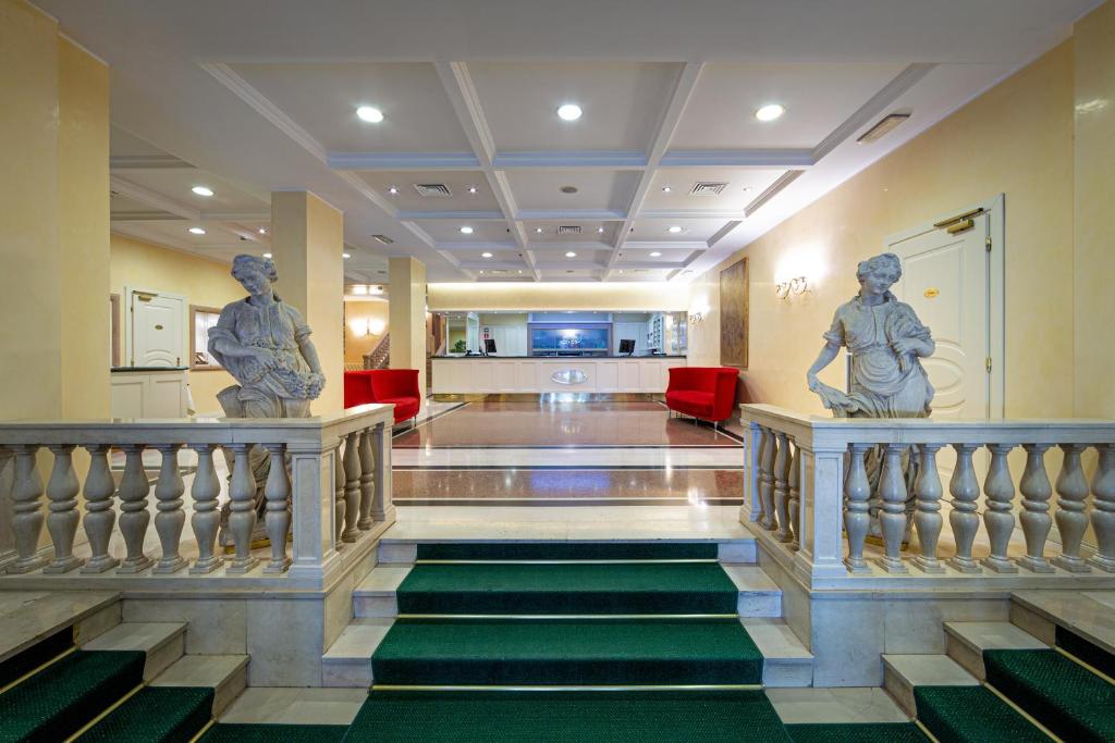 - un hall avec deux statues de personnes sur les escaliers dans l'établissement Ambassador Palace Hotel, à Udine