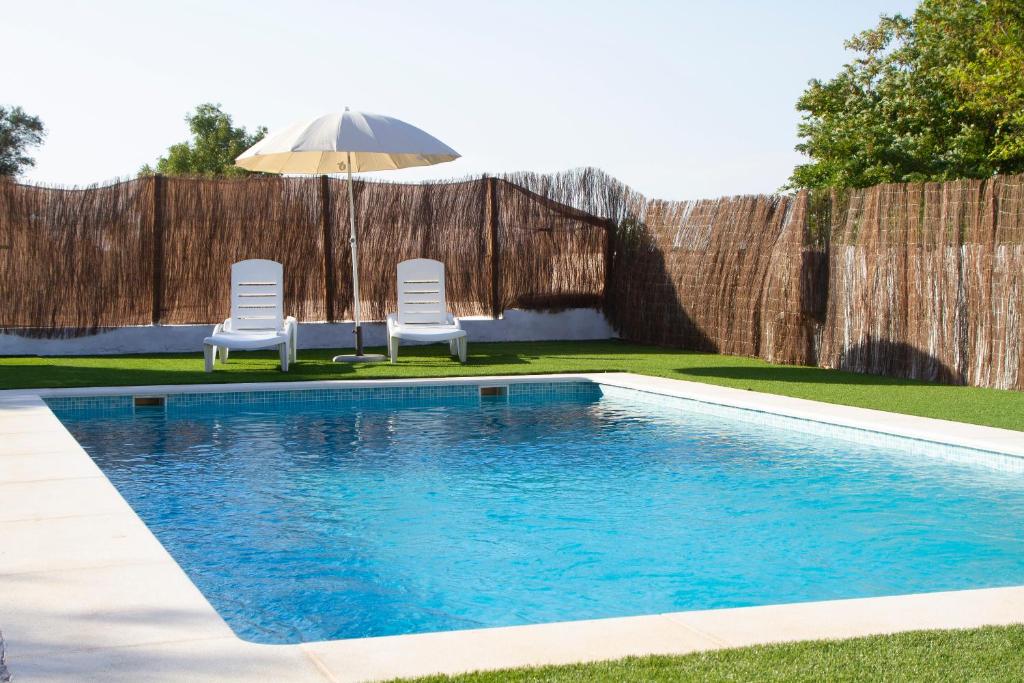 a swimming pool with two chairs and an umbrella at Vivienda Rural Cortijo de Liche in Arcos de la Frontera