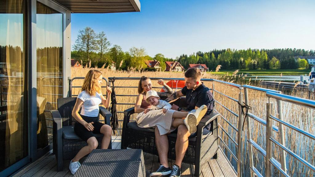 a group of people sitting on a deck with a baby at Domek na wodzie Topiko Czarter przy Hotelu Ognisty Ptak in Ogonki