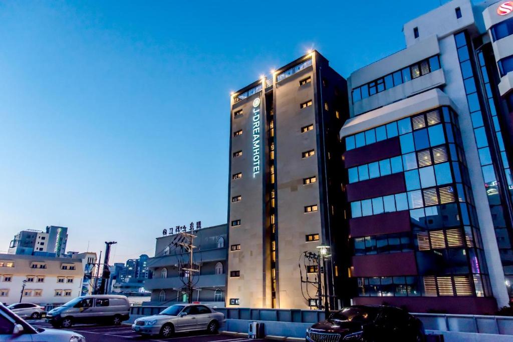 a tall building with cars parked in a parking lot at Index Hotel J Dream Jeju in Jeju