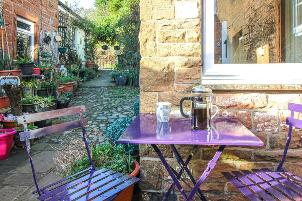 een paarse tafel met een kruik naast twee banken bij 2 Eden Grove Cottages in Armathwaite