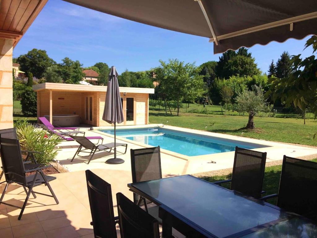 un patio con tavolo, sedie e piscina di Villa de 4 chambres avec piscine privee spa et jardin clos a Prayssac a Prayssac