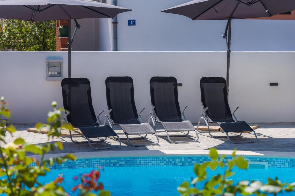 une rangée de chaises et de parasols à côté d'une piscine dans l'établissement Apartments Baldo, à Vodice