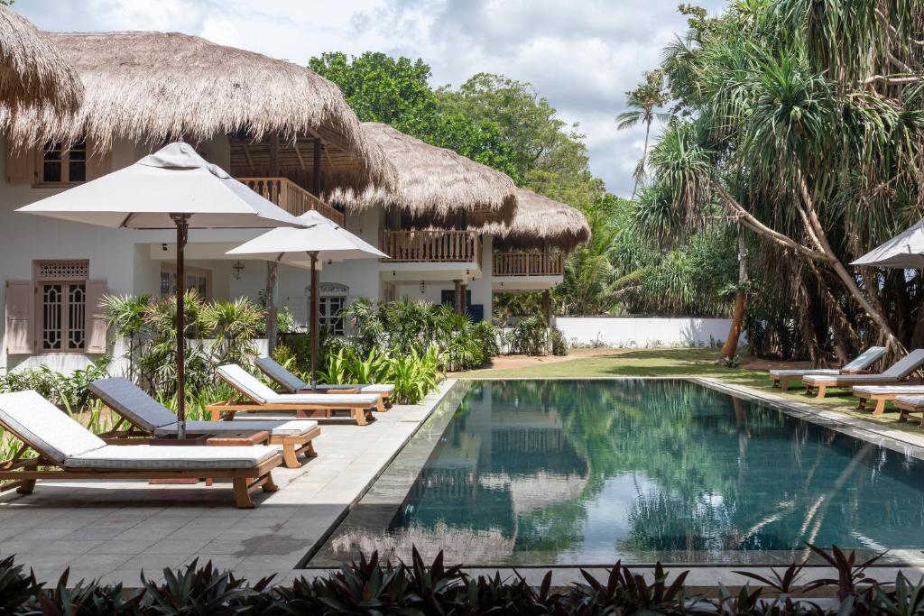 a resort pool with chairs and umbrellas at Halcyon Mawella in Tangalle