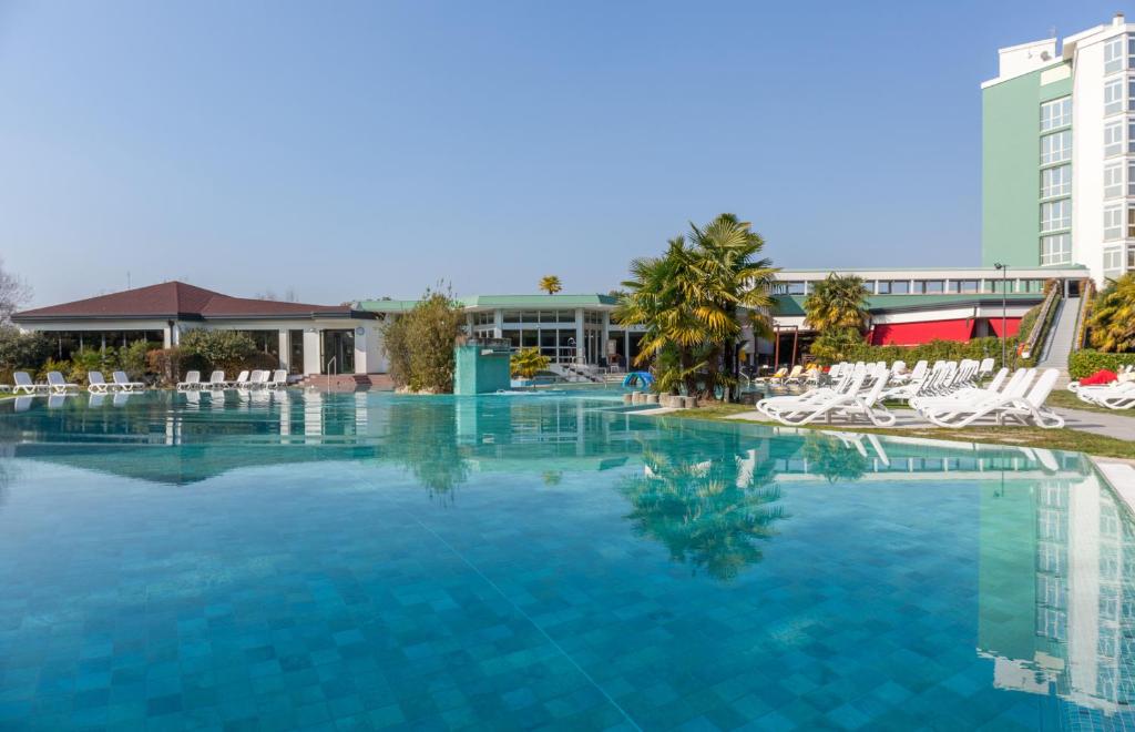 a large swimming pool with white chairs and a building at Hotel Garden Terme in Montegrotto Terme