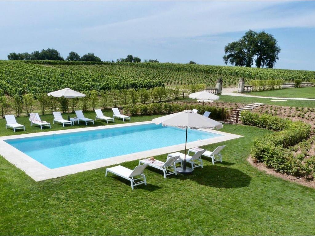 una piscina en un campo con sillas y sombrillas en Magnifique villa plain pied avec piscine en Fronsac