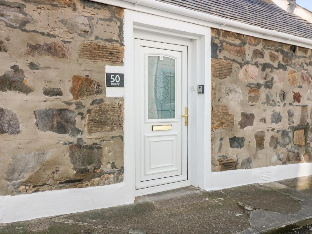 una puerta blanca con una señal en el lateral de un edificio de piedra en Seaspray Cottage en Buckie