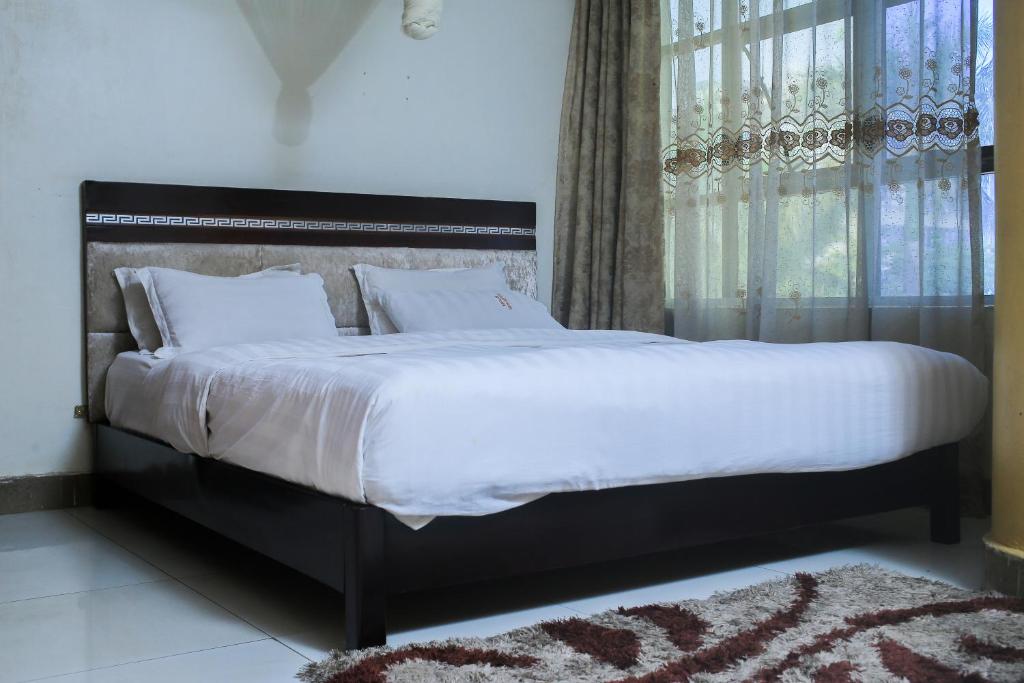 a bedroom with a large bed with white sheets and a window at Steric Hotel Kampala in Kampala