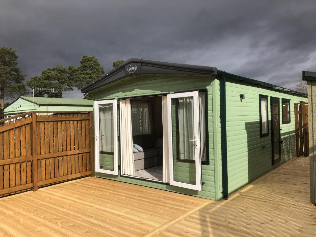 ein kleines grünes Haus auf einer Holzterrasse in der Unterkunft Luxury 2 bedroom caravan in stunning location in Pitlochry