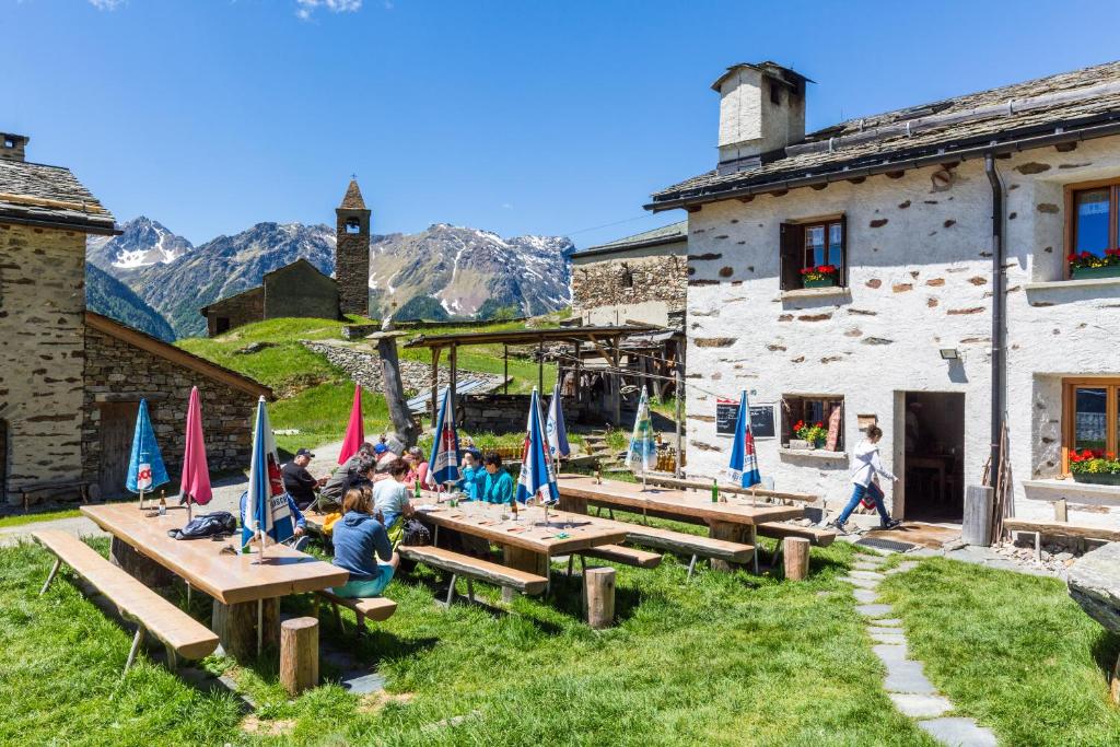 um grupo de pessoas sentadas em mesas de piquenique em frente a um edifício em Rifugio Alpe San Romerio em Brusio