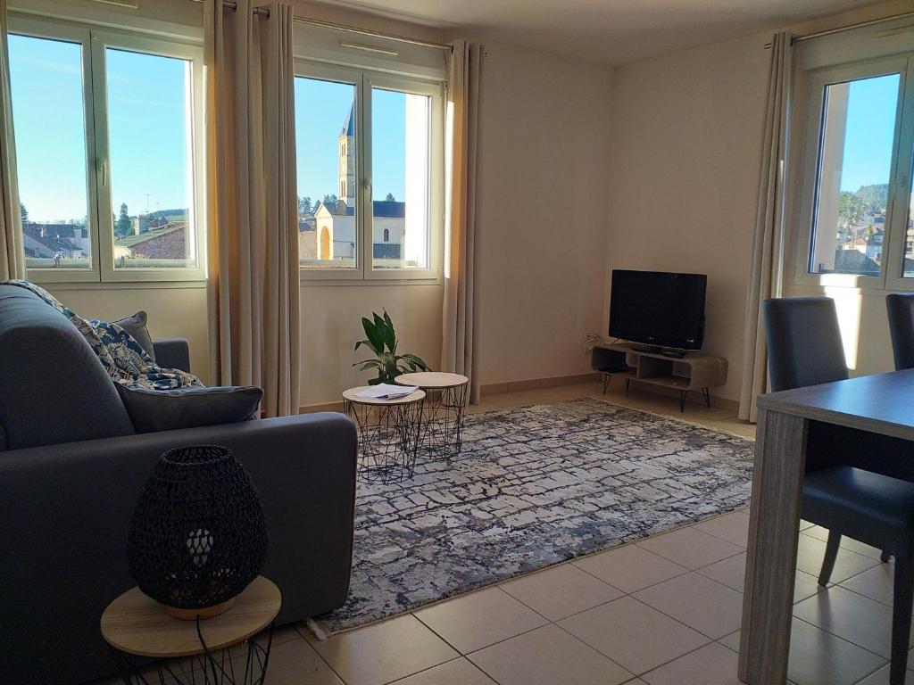 ein Wohnzimmer mit einem Sofa, einem TV und Fenstern in der Unterkunft Apppartement 2 pièces centre-ville in Chauffailles