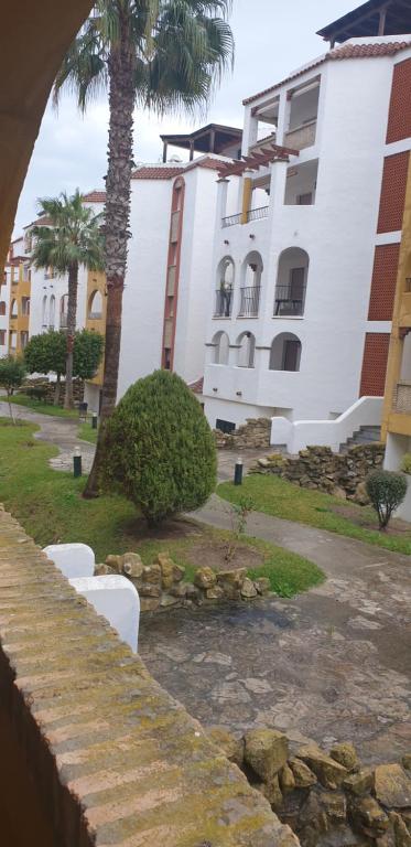 a large white building with palm trees in front of it at Apartamentos Atlanterra COSTA Y SOL in Zahara de los Atunes