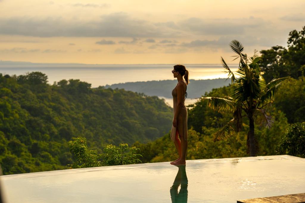 a woman standing on the edge of a wall looking out at the ocean at Tanah Damai Hotel in Nusa Penida